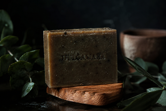 Handmade tallow soap bar surrounded by eucalyptus leaves on dark wood, photographed in a moody artisanal setting that evokes traditional men’s grooming and natural soapmaking.